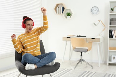 Photo of Happy woman in headphones enjoying music and dancing on cosy armchair at home