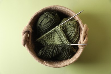 Photo of Knitting, needles and soft yarns on light green background, top view
