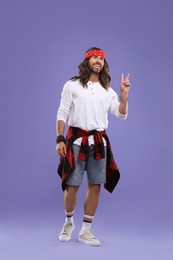 Photo of Stylish hippie man showing V-sign on violet background