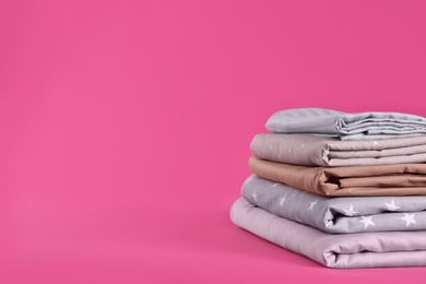 Photo of Stack of clean bed sheets on pink background. Space for text