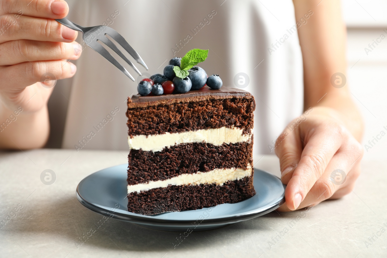 Photo of Woman with slice of chocolate sponge berry cake at table, closeup