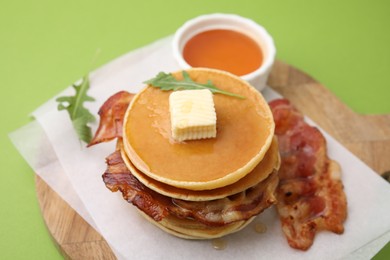 Photo of Delicious pancakes with bacon, butter, arugula and honey on green table, closeup