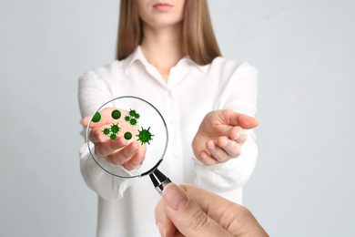 Image of Woman detecting bacteria with magnifying glass on light background, closeup. Prevention disease