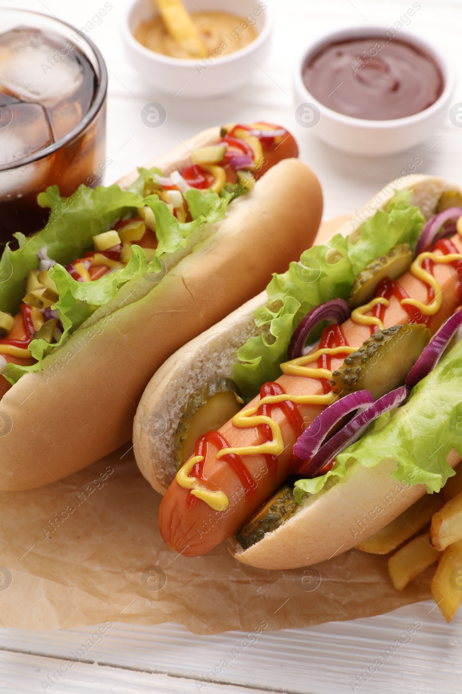 Photo of Delicious hot dogs with lettuce, onion and pickle on white wooden table, closeup