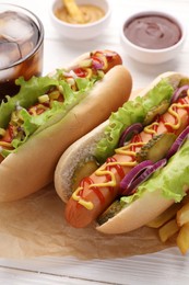 Photo of Delicious hot dogs with lettuce, onion and pickle on white wooden table, closeup