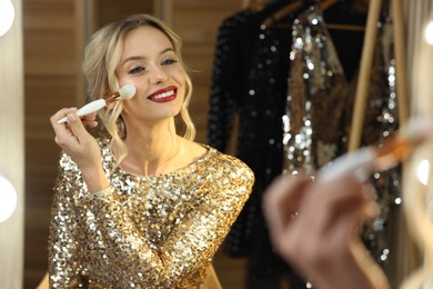 Photo of Beautiful makeup. Smiling woman applying powder with brush onto face in front of mirror in dressing room