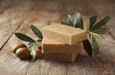 Handmade soap bars and leaves with olives on wooden table