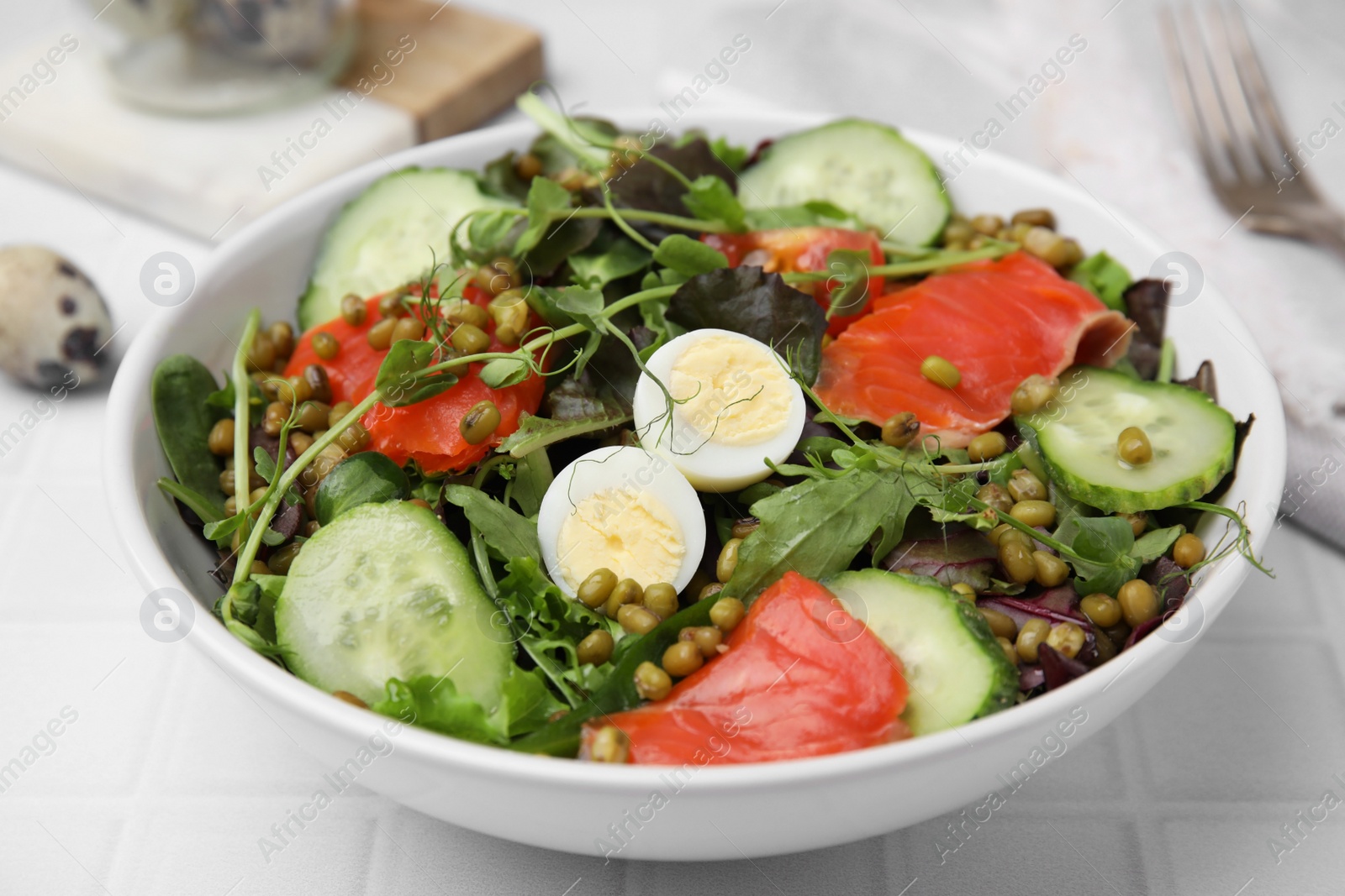 Photo of Bowl of salad with mung beans on white tiled table, closeup