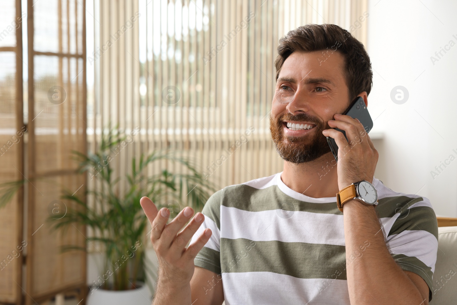 Photo of Handsome man talking on smartphone at home, space for text