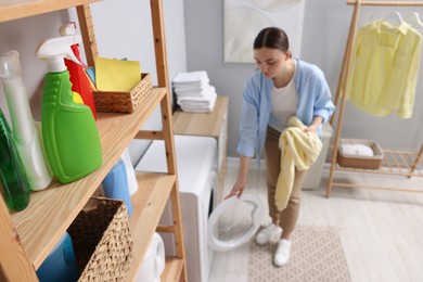 Beautiful woman putting sweatshirt into washing machine in laundry room, selective focus