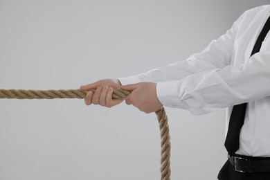 Dispute concept. Businessman pulling rope on light grey background, closeup