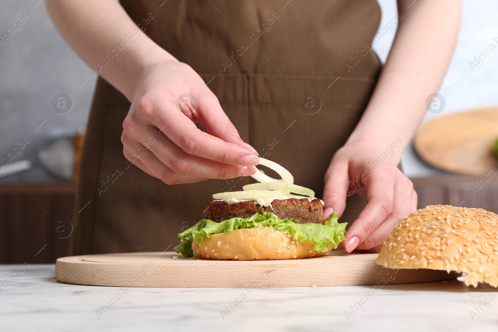 Photo of Woman making delicious vegetarian burger at white marble table, closeup