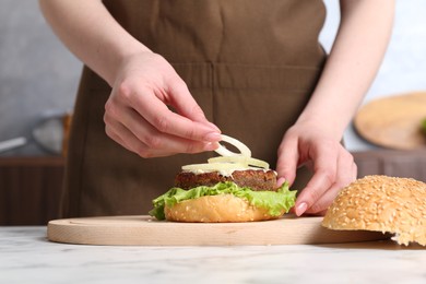 Photo of Woman making delicious vegetarian burger at white marble table, closeup