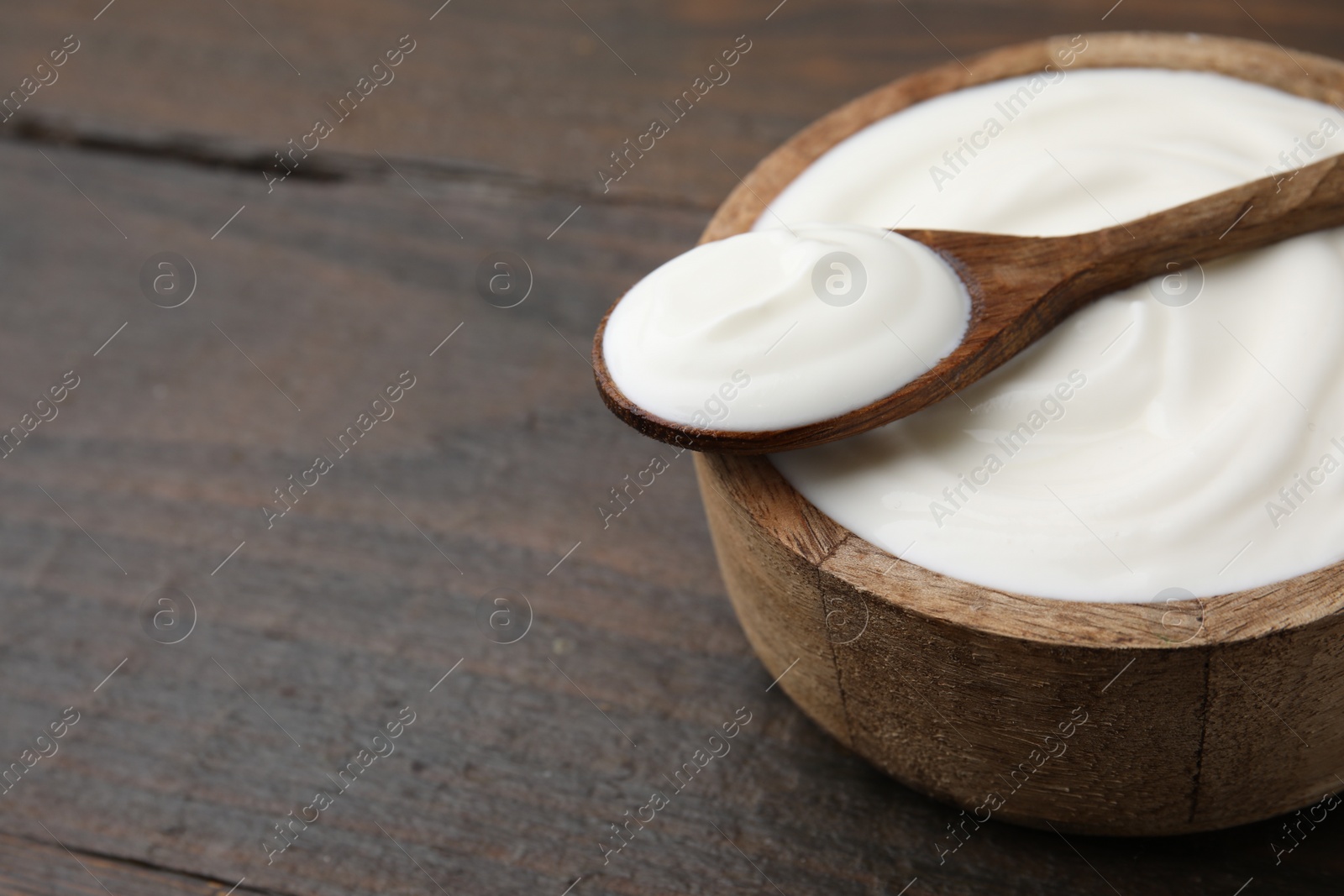 Photo of Delicious natural yogurt in bowl and spoon on wooden table, closeup. Space for text