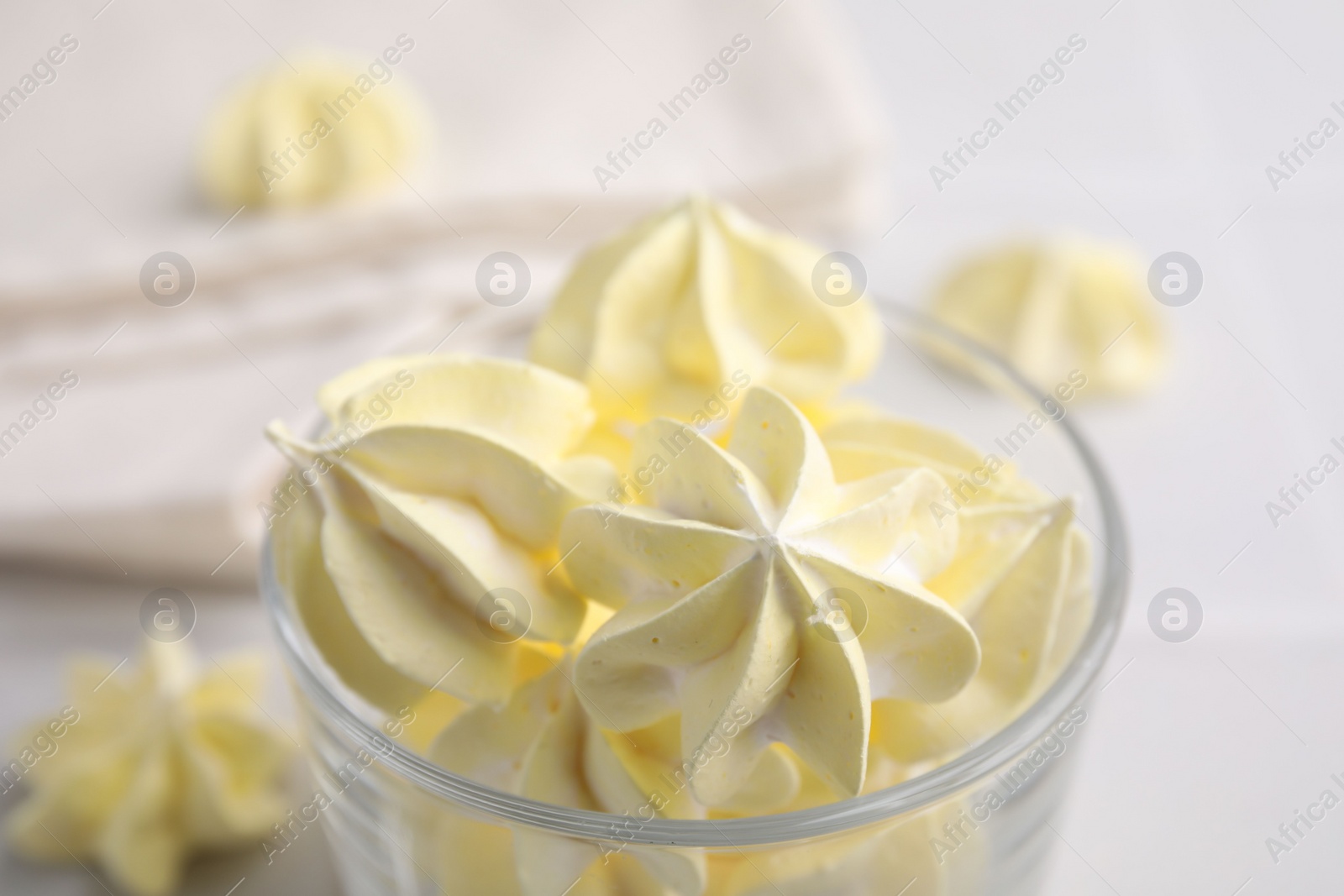 Photo of Tasty meringue cookies in glass on white table, closeup