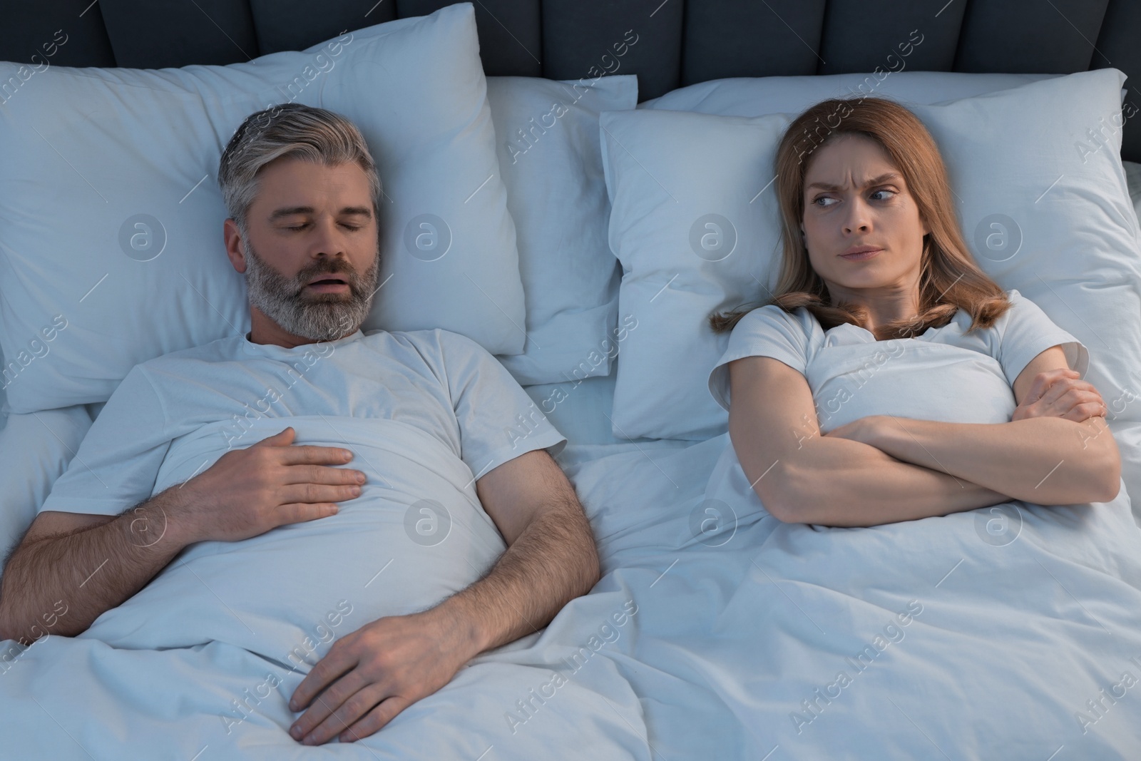 Photo of Irritated woman lying near her snoring husband in bed at home