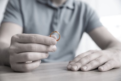 Man with wedding ring at table indoors, closeup. Cheating and breakup