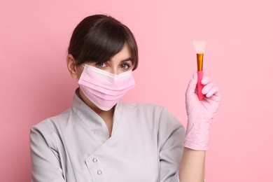Photo of Cosmetologist with silicone cosmetic brush on pink background