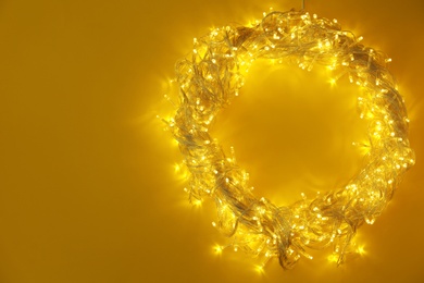 Photo of Frame made of glowing Christmas lights on yellow background, top view. Space for text