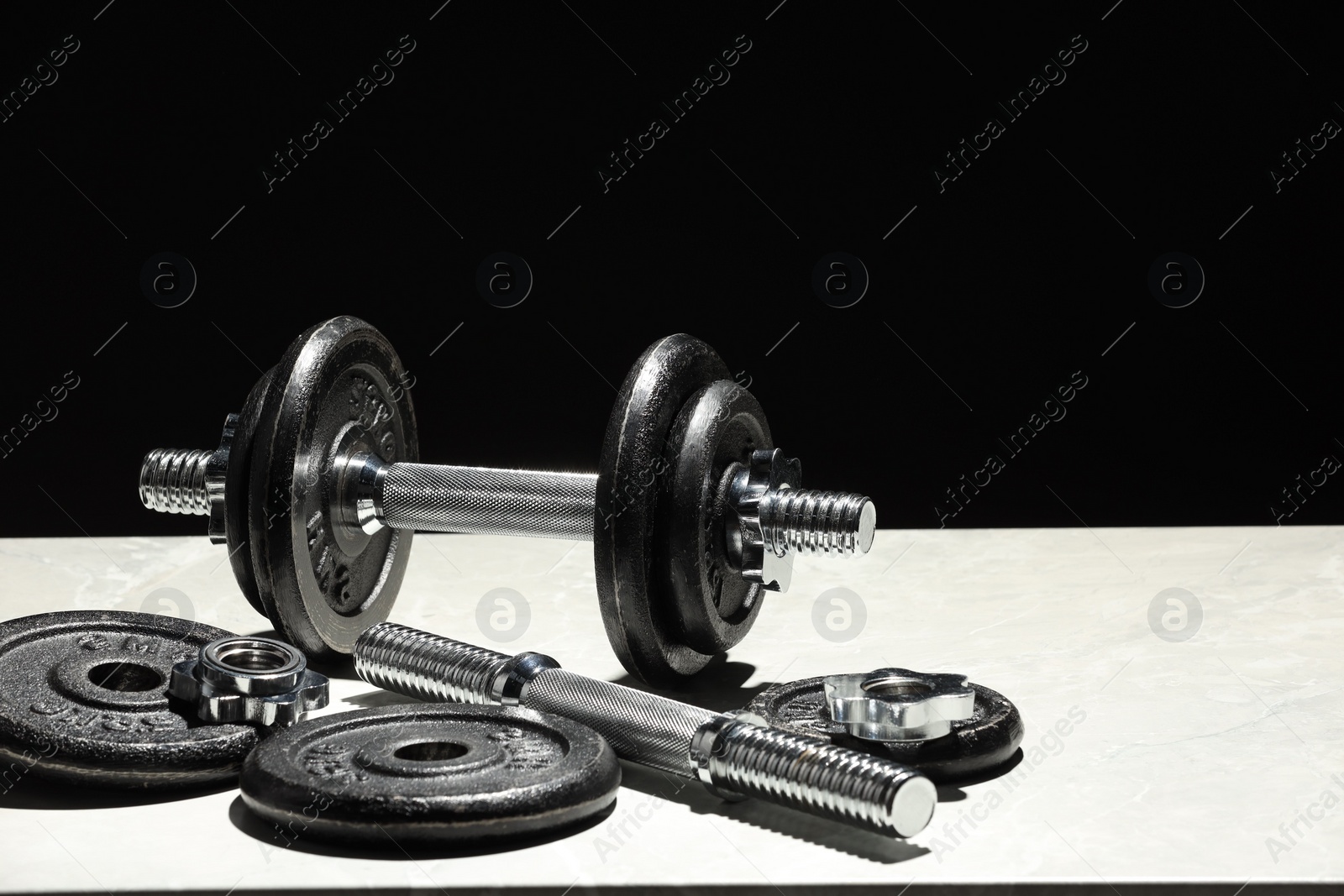 Photo of Barbell and parts of one on light table against black background. Space for text