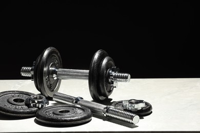 Barbell and parts of one on light table against black background. Space for text