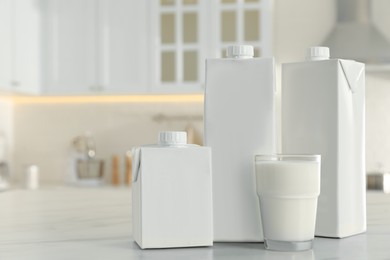 Photo of Carton boxes and glass of milk on table in kitchen, space for text