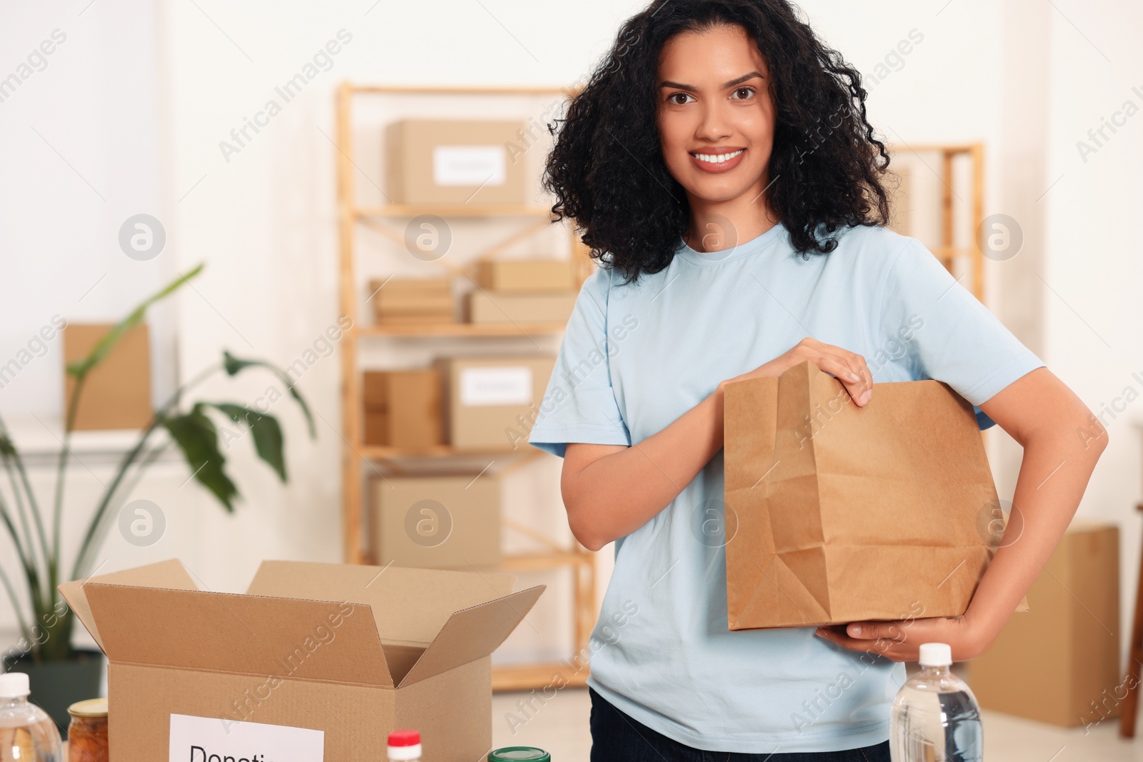 Photo of Volunteering. Happy woman with paper bag in warehouse