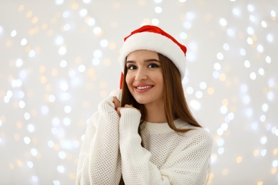 Happy young woman in Santa hat against blurred Christmas lights