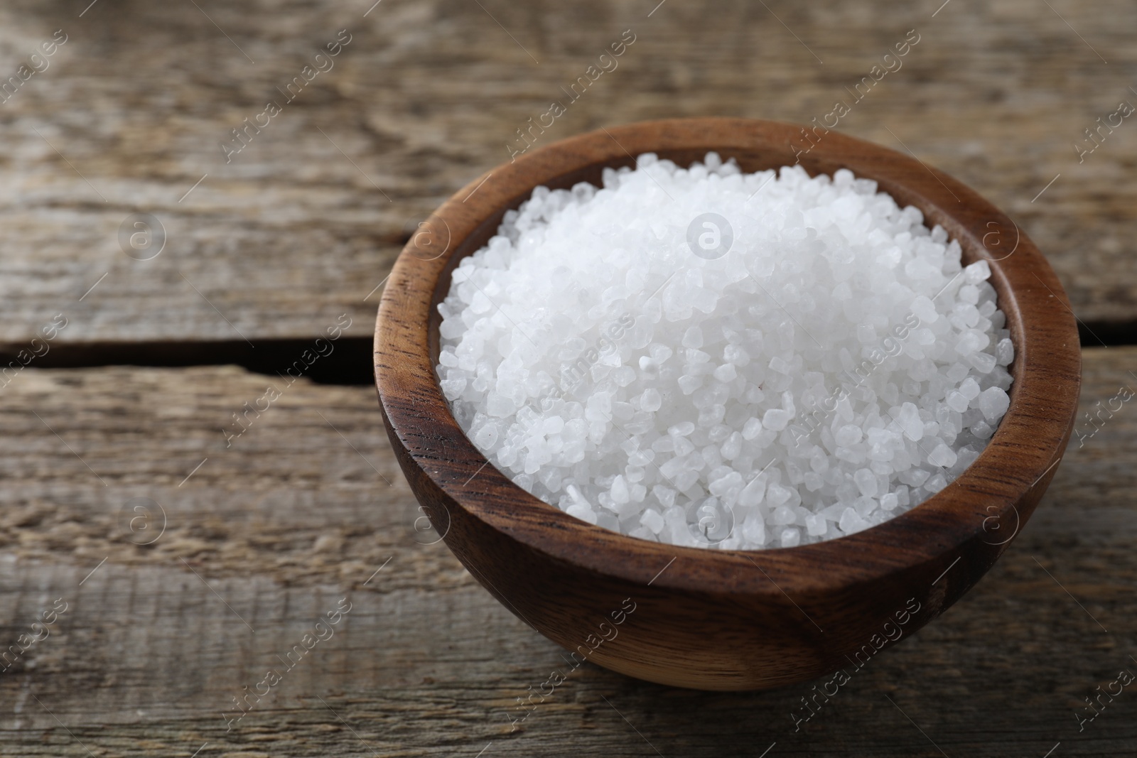 Photo of Organic salt in bowl on wooden table, closeup. Space for text