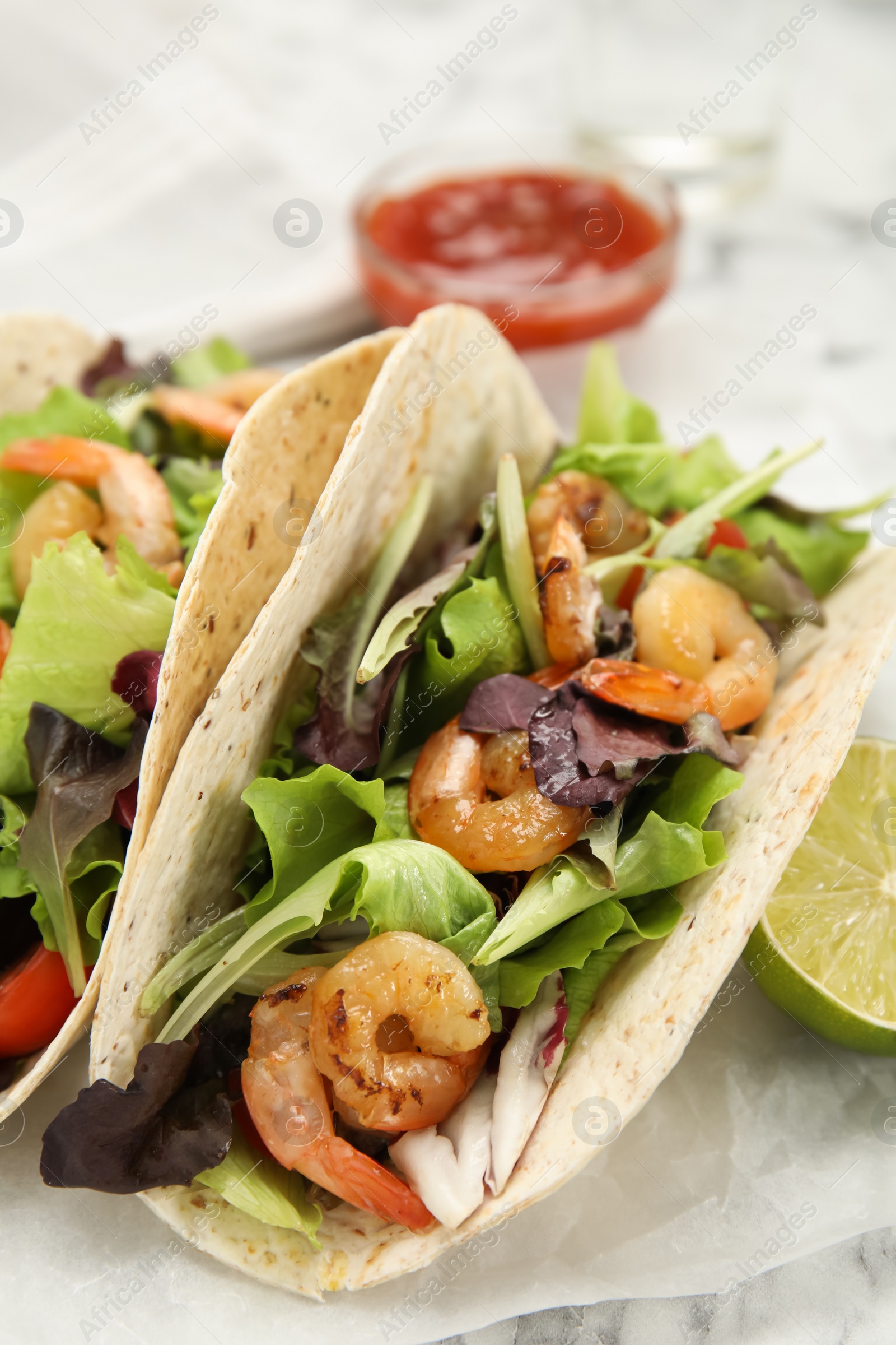 Photo of Delicious tacos with shrimps and lime on white table, closeup