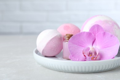 Photo of Colorful bath bombs, bottle of oil and orchid flower on grey table, closeup