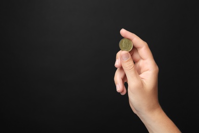 Young woman holding coin on black background, closeup view. Space for text