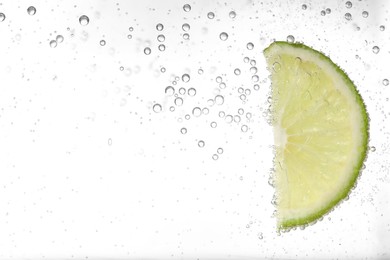 Photo of Juicy lime slice in soda water against white background, closeup. Space for text