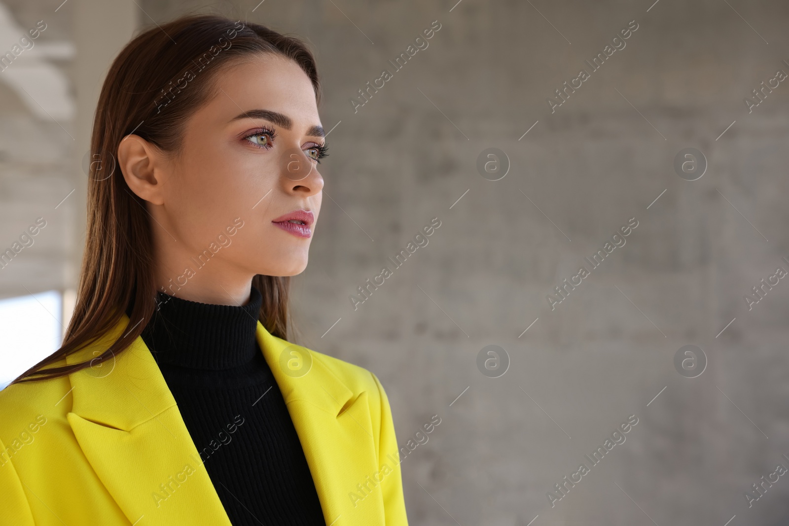 Photo of Fashionable young woman in stylish outfit with yellow jacket near grey wall. Space for text