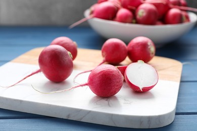 Photo of Board with fresh ripe radishes on blue wooden table, closeup