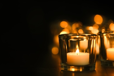 Burning candle on table in darkness, space for text. Funeral symbol