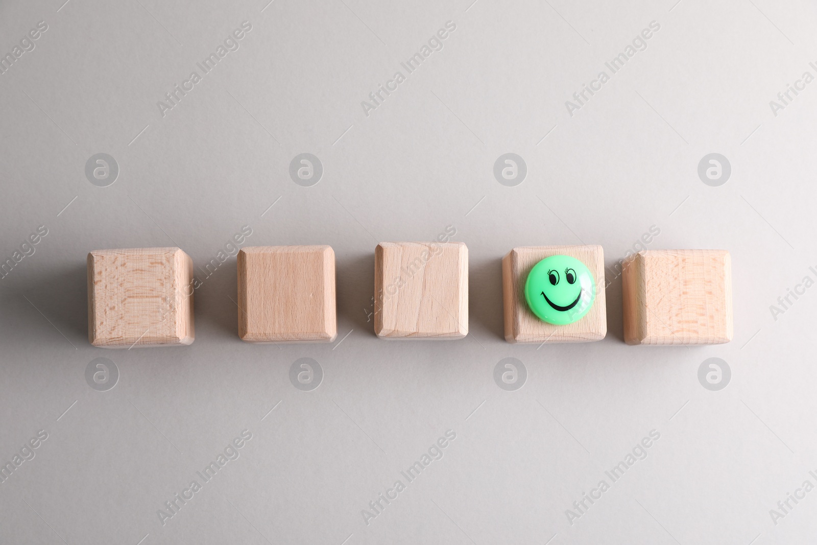 Photo of Choice concept. Green magnet with happy emoticon on wooden cube among ones on light grey background, flat lay