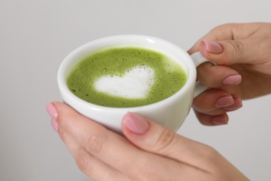 Photo of Woman with cup of delicious matcha latte on light background, closeup