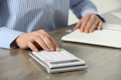 Professional accountant using calculator at wooden desk in office, closeup