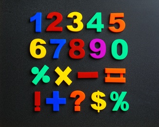 Photo of Colorful magnetic numbers and math symbols on black background, top view