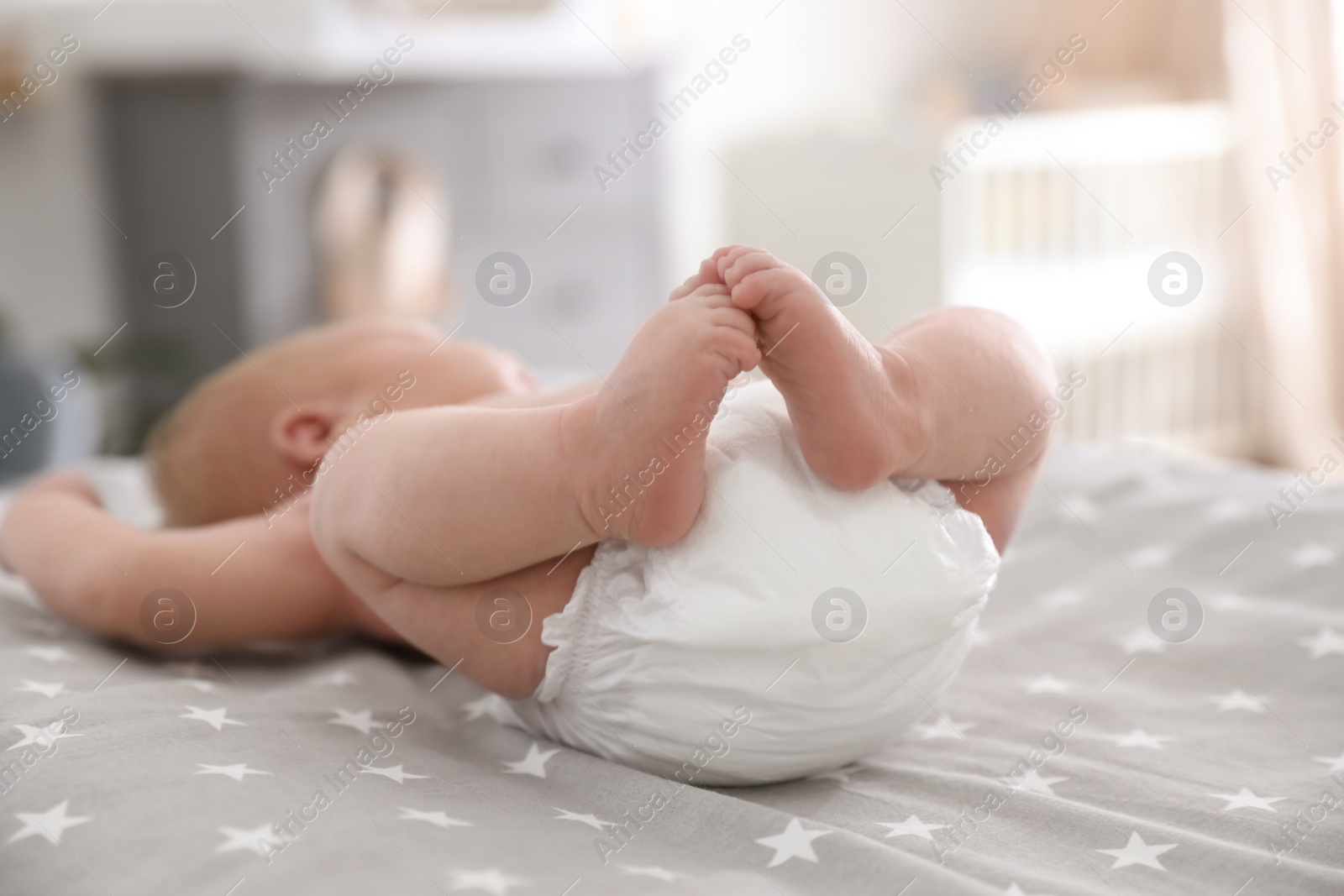 Photo of Cute little baby in diaper lying on bed in room, closeup