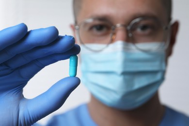 Photo of Doctor holding pill on light background, selective focus. Space for text