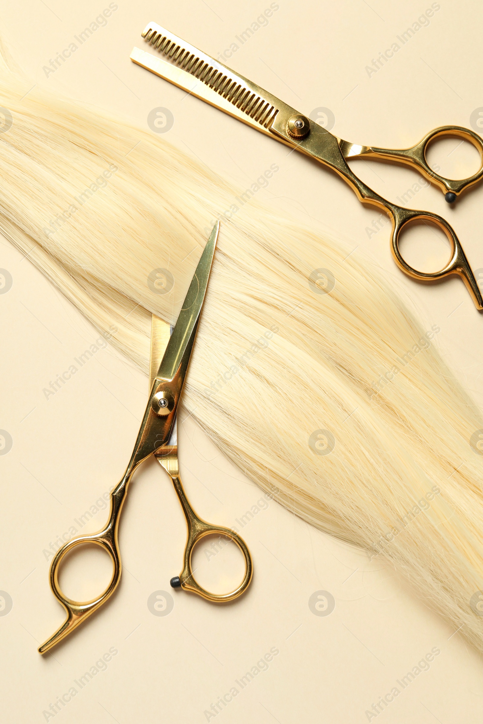 Photo of Professional scissors with blonde hair strand on beige background, flat lay