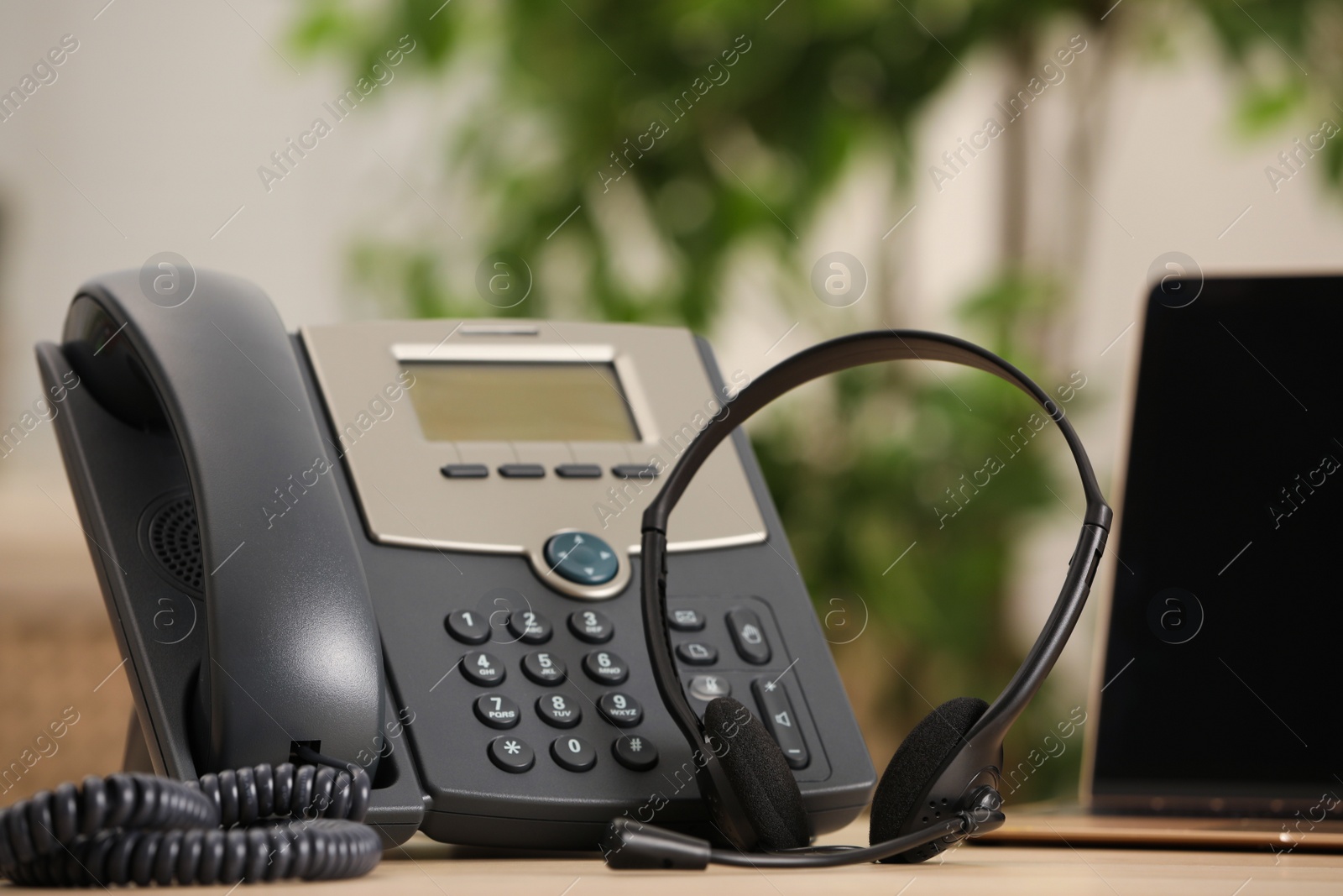 Photo of Headset, desktop telephone and laptop on table indoors. Hotline concept