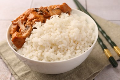 Bowl of delicious rice with meat, mushrooms and chopsticks on table, closeup