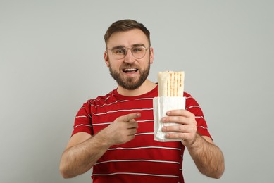 Young man with delicious shawarma on grey background