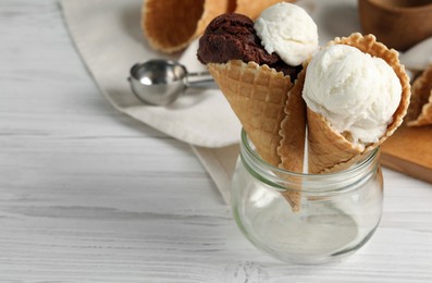 Photo of Ice cream scoops in wafer cones on white wooden table, space for text