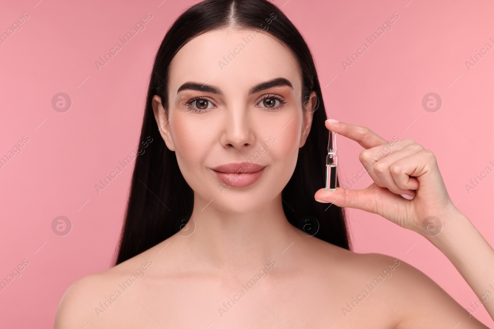 Photo of Beautiful young woman holding skincare ampoule on pink background