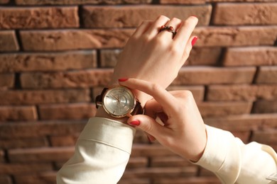 Woman wearing luxury wristwatch near brick wall, closeup