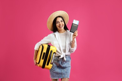 Photo of Happy female tourist with suitcase, ticket and passport on pink background